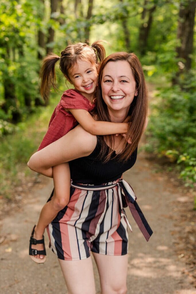 Melissa Sampson smiling for the camera with her happy daughter sitting on her back. 