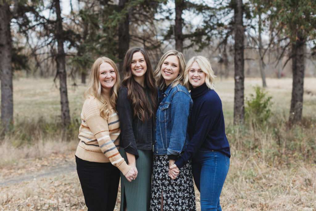 Four women smiling and holding hands during a fall photo session in the woods at Lindenwood Park.