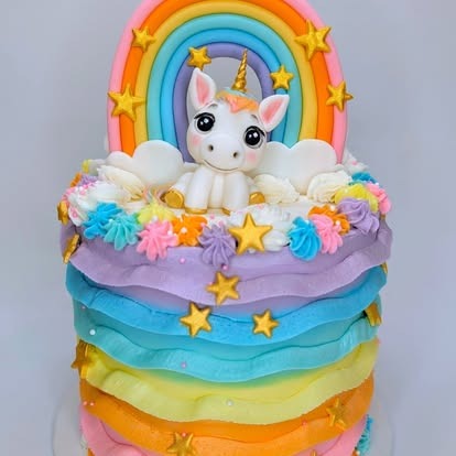 A colorful rainbow-layered cake topped with a fondant unicorn and golden stars.

