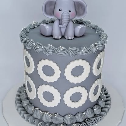 A gray and white cake topped with a fondant baby elephant and decorative circular patterns.