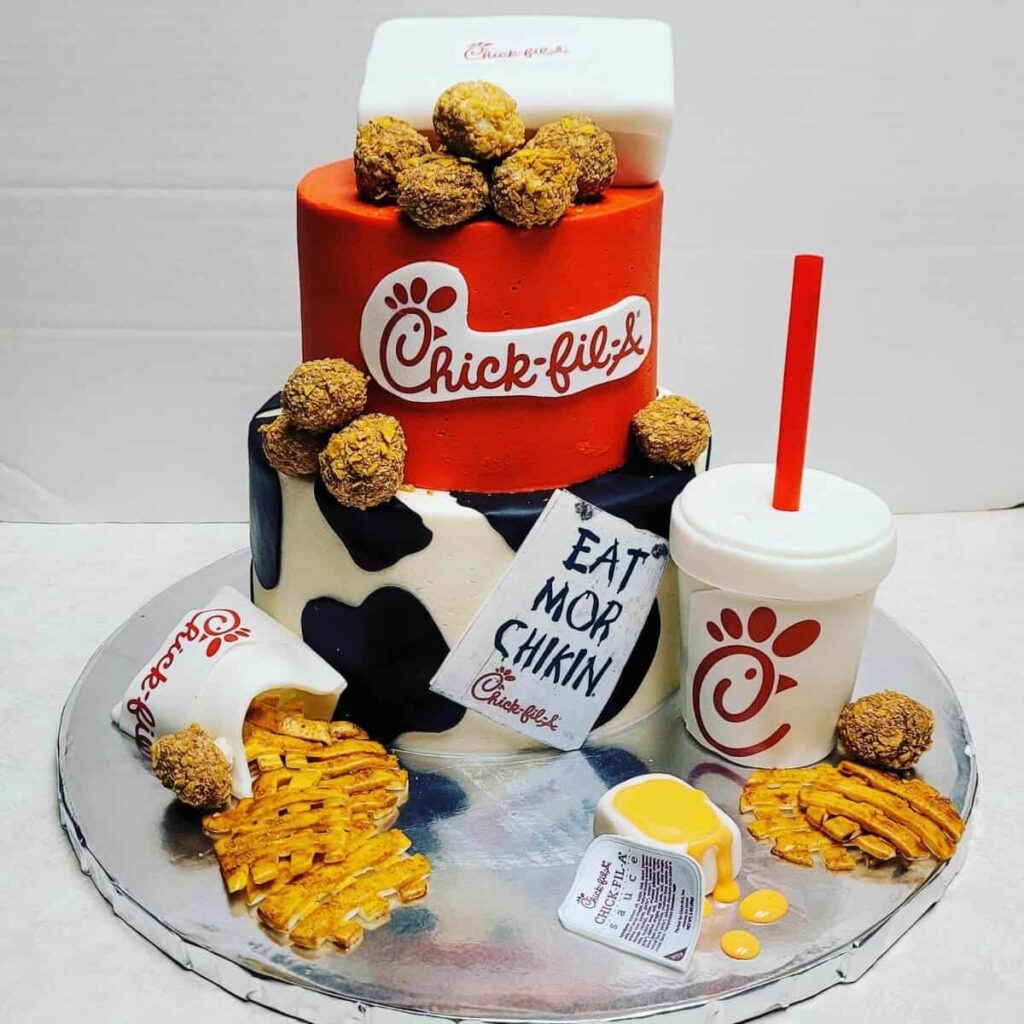 A detailed Chick-fil-A-themed cake featuring chicken nuggets, fries, a drink, and sauce, all made from fondant.