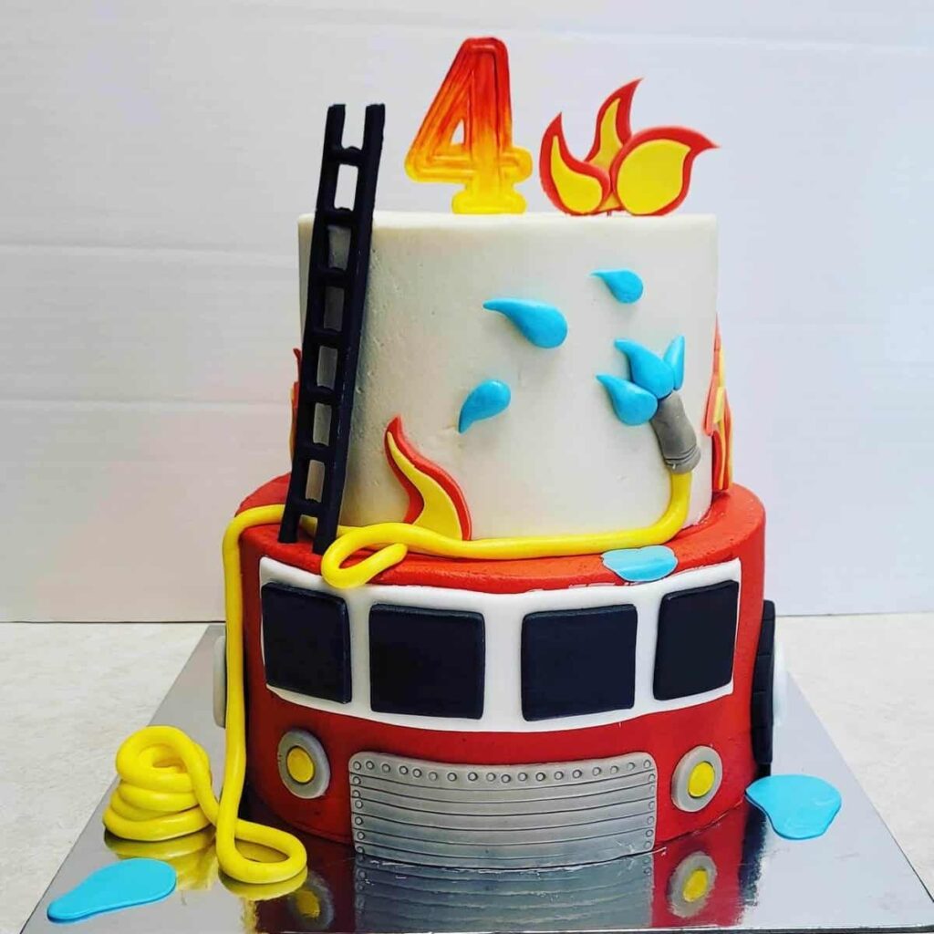 A two-tier firetruck-themed birthday cake with flames, water droplets, and a ladder, topped with the number 4.