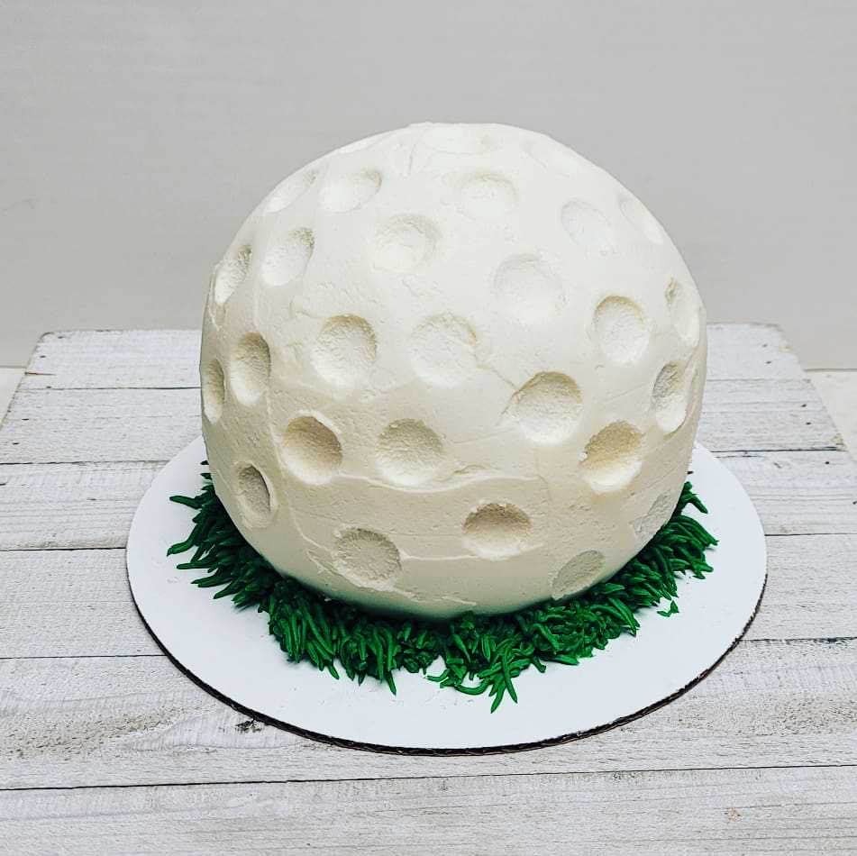 A round cake designed to look like a textured golf ball sitting on green frosting “grass.”