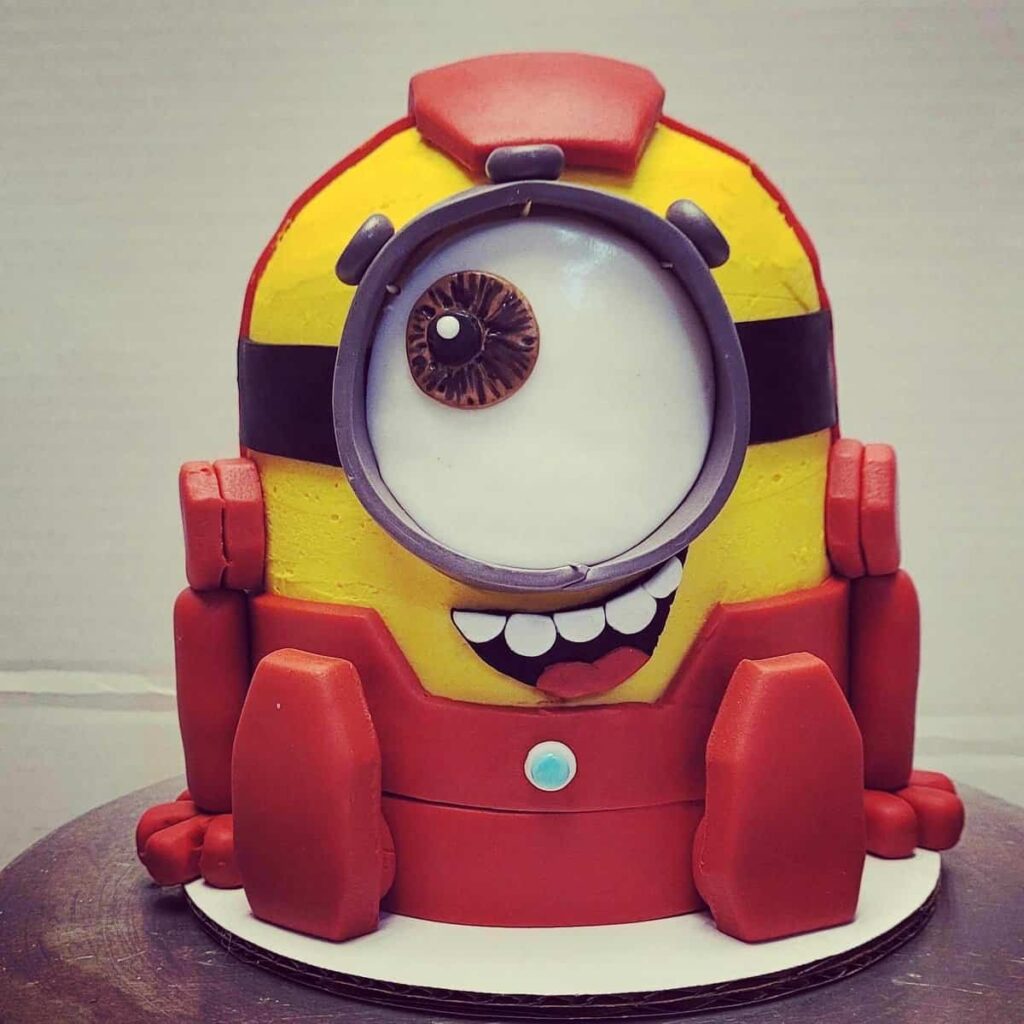 A 3D cake shaped like a mash-up of a Minion and Iron Man, with detailed fondant features.
