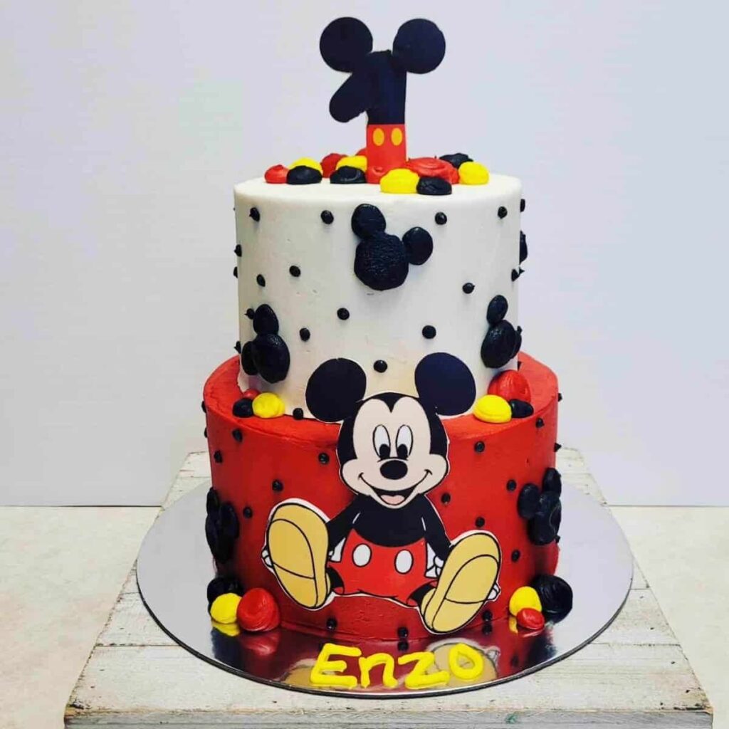 A Mickey Mouse birthday cake in red, white, and black, decorated with Mickey ears and the name "Enzo."