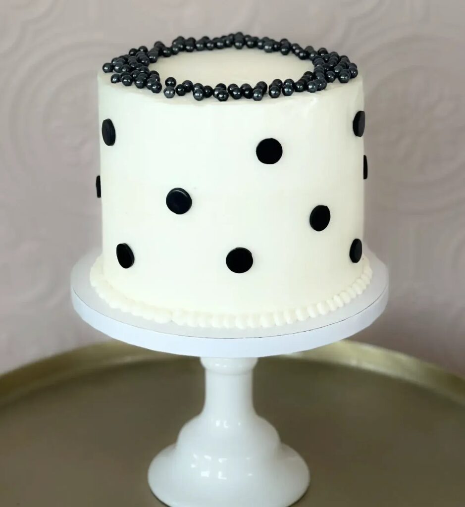 A simple white cake with black polka dots and a border of shiny black pearls on top.

