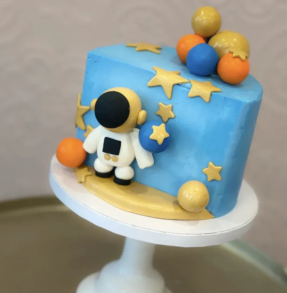 A blue cake with fondant stars, planets, and a little astronaut figure standing on the side.