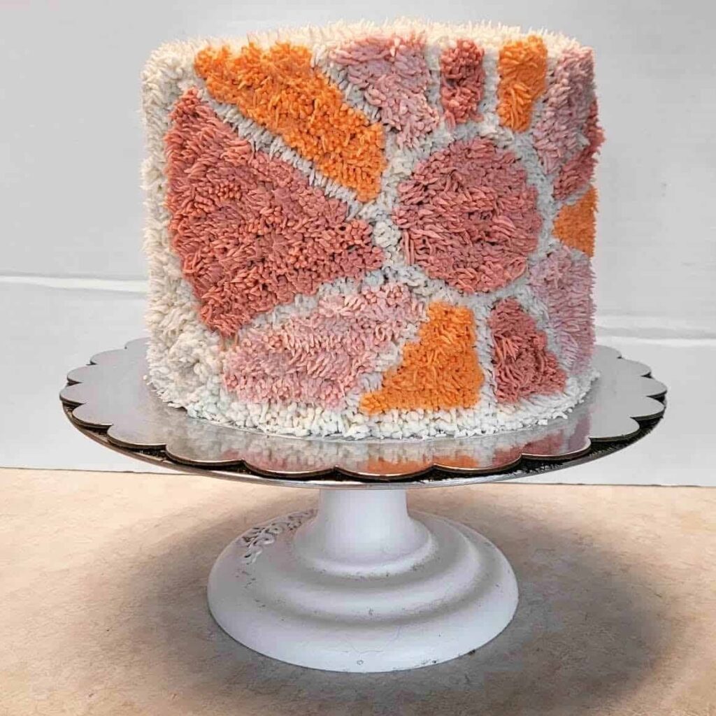 A cake with shaggy, textured buttercream in a geometric pattern inspired by retro rug designs.