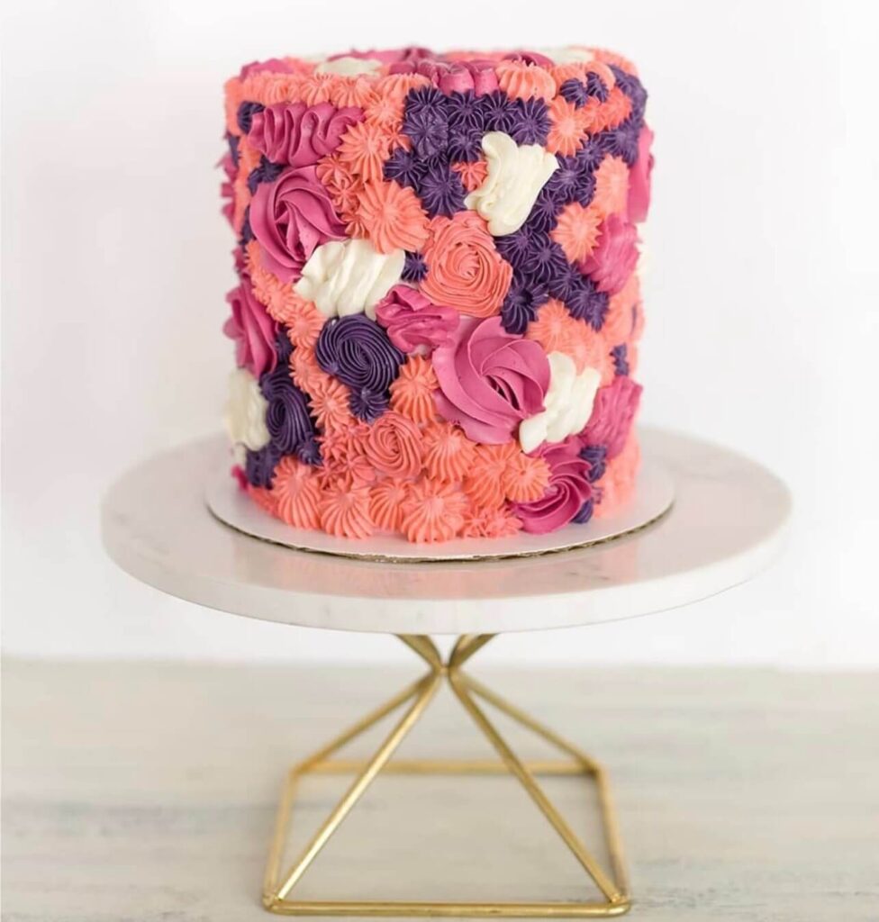 A pink, purple, and white buttercream cake covered in intricate piped rosettes and floral patterns.

