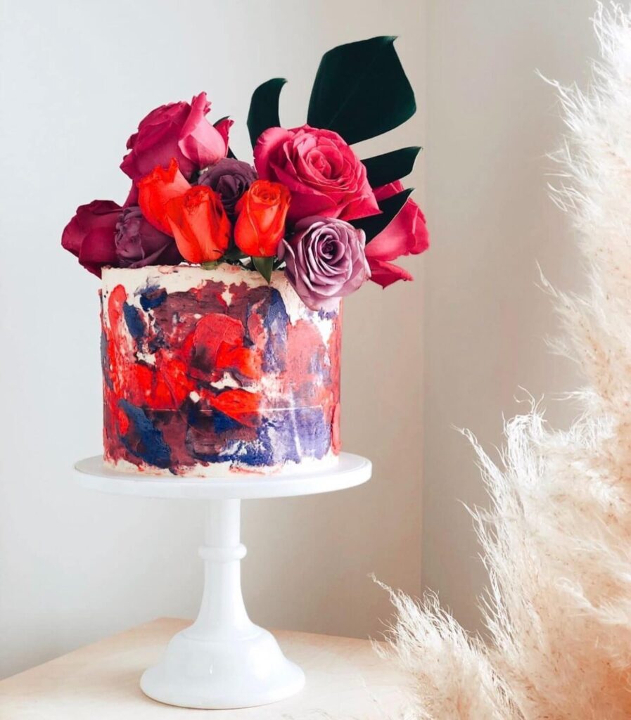 A brightly colored cake with a watercolor-style frosting and decorated with small white flowers and pearl sprinkles.