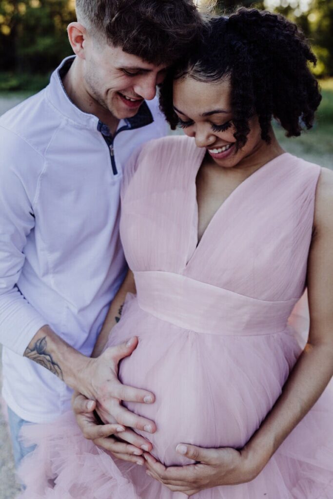 A couple looks lovingly at the woman's baby bump while placing their hands over it during a maternity shoot.