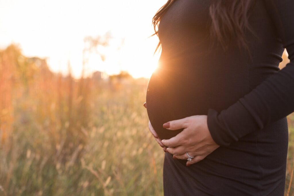 Close-up of a pregnant belly in a black dress, with the sun glowing through the background.