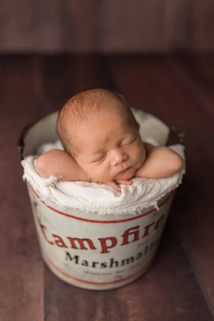 Sleeping newborn baby posed in a vintage tin bucket prop with soft fabric support