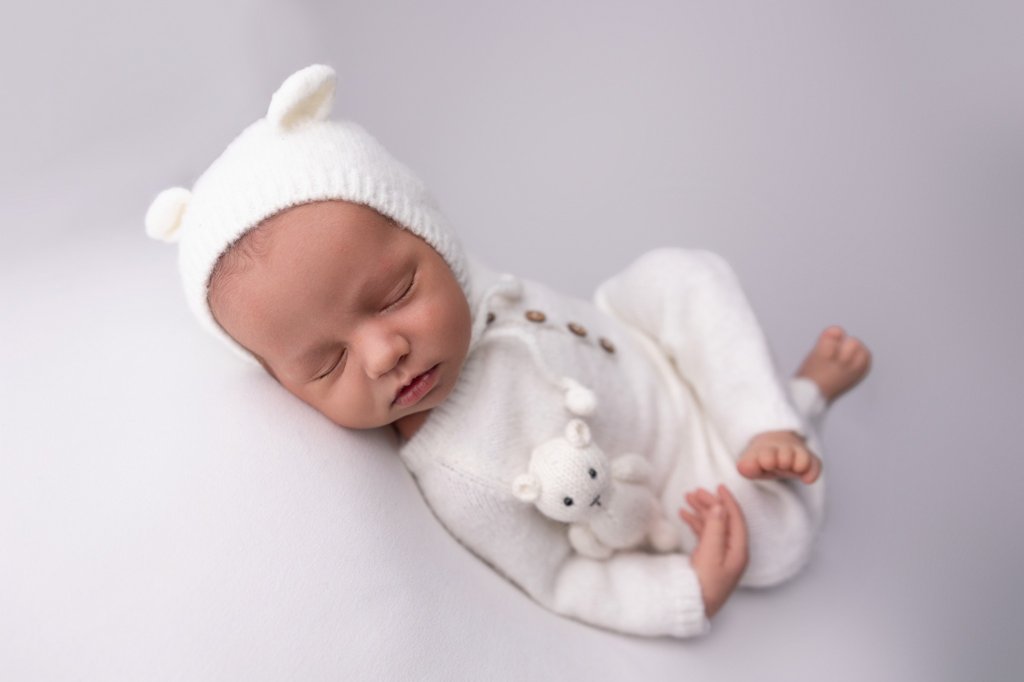 Sleeping baby wearing a white baby outfit and bonnet. 