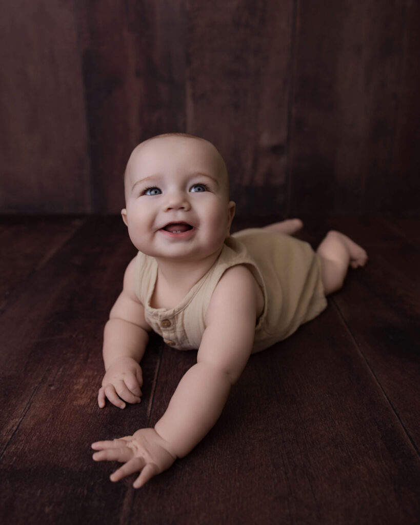 Happy baby lying on a wooden floor and smiling during a milestone photography session.