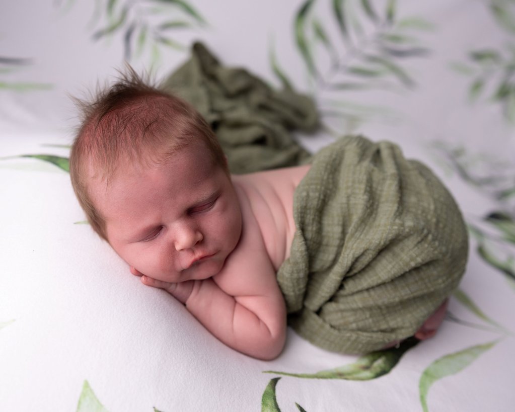 Sleeping baby wrapping in a green wrap on a soft blanket with leaves. 