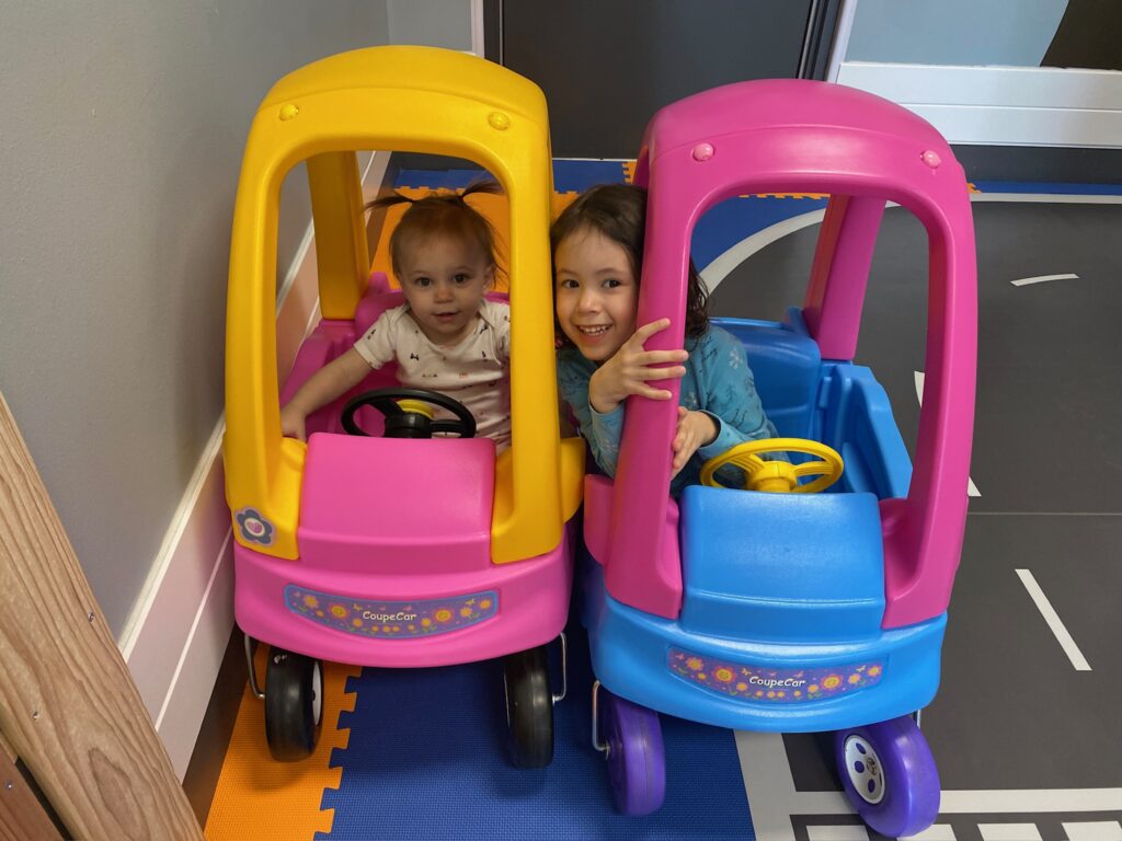 Children sitting in colorful toy cars inside the toddler play area at Dreamland Indoor Playground.