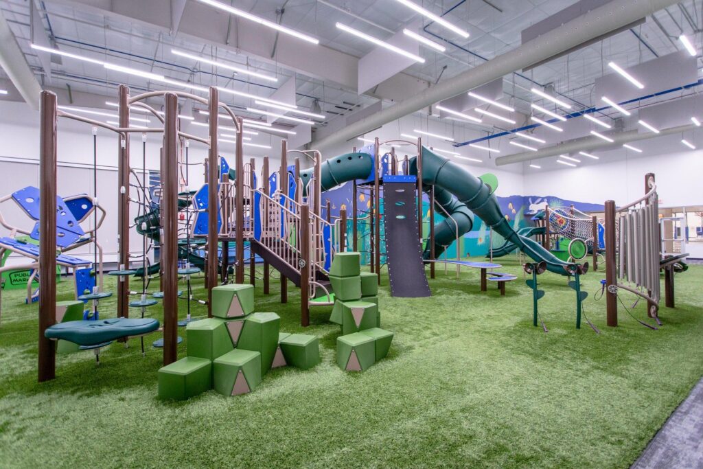 Indoor playground and climbing structure at Fargo Parks Sports Center with slides, obstacle equipment and artificial turf flooring.