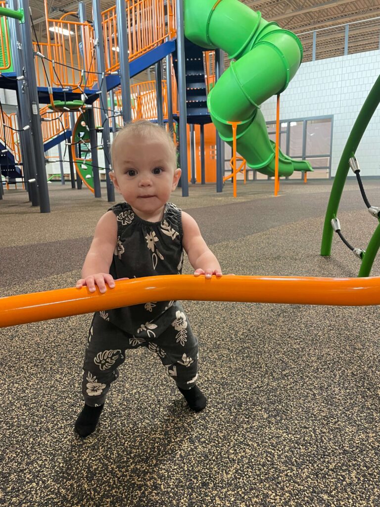 Toddler standing near playground equipment and slides inside the Rustad Recreation Center indoor play area.